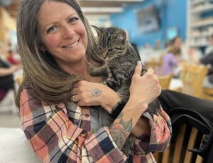 Woman smiling and holding a tabby kitten indoors.